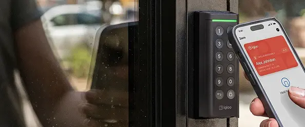 Hand holding a phone with an igloo mobile key up to a black igloo keypad reader on a glass entrance door
