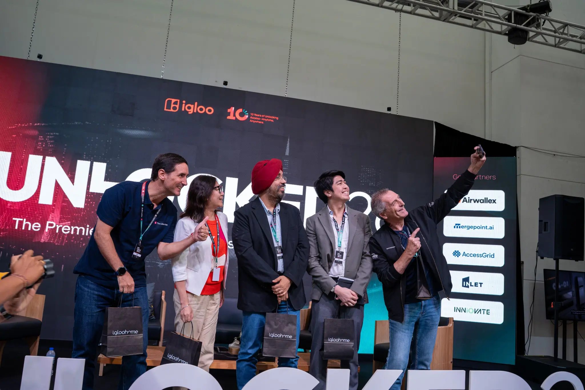Speakers smiling on stage under the UNLOCKED26 banner and partner logos