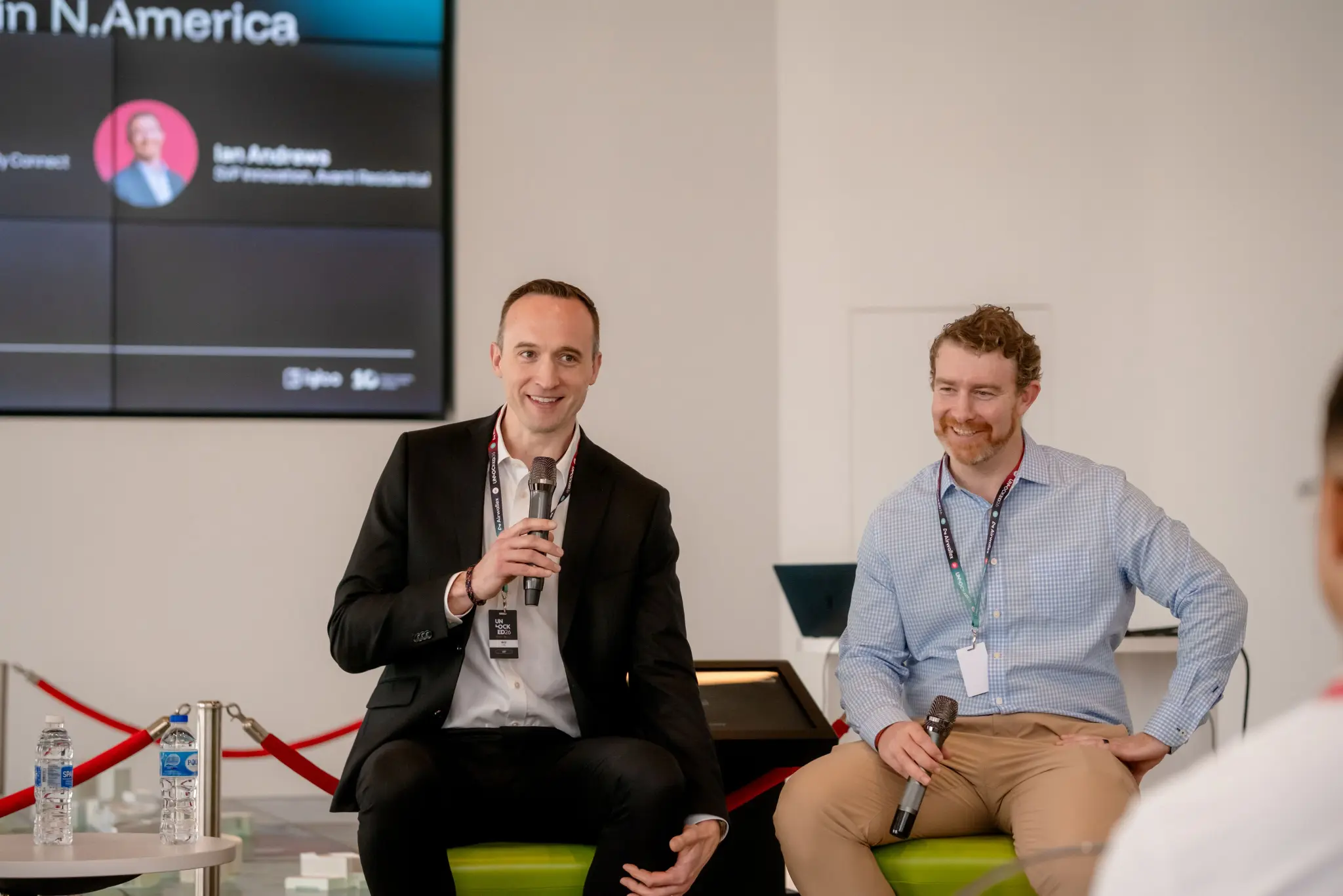 Two panellists with microphones on a North America fireside chat at UNLOCKED26