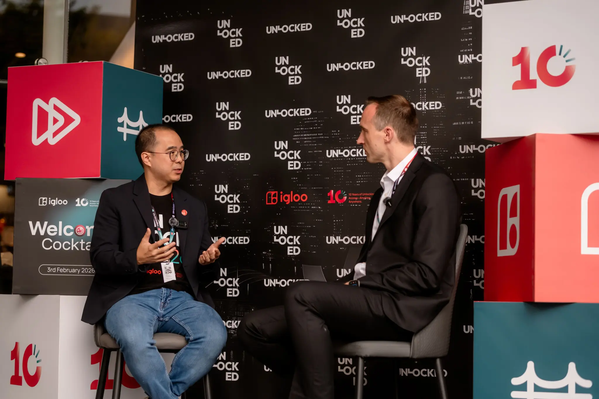 Two guests in conversation in front of the UNLOCKED26 media wall