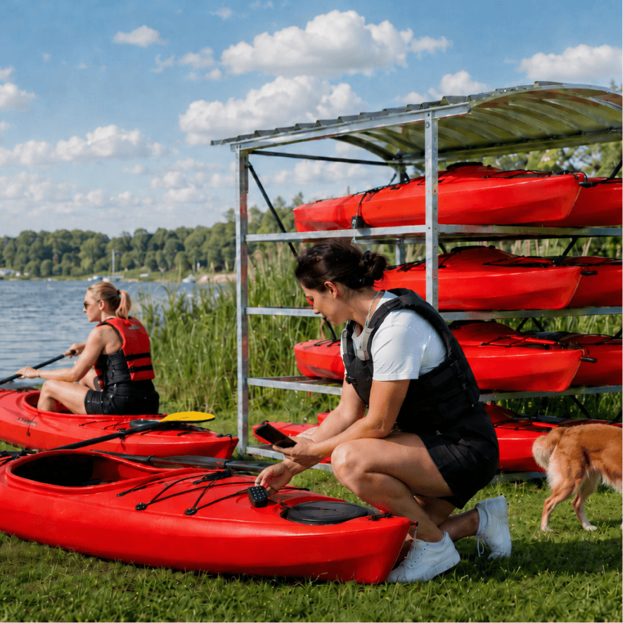Two guests unloading kayaks from a lakeside self-serve rental rack