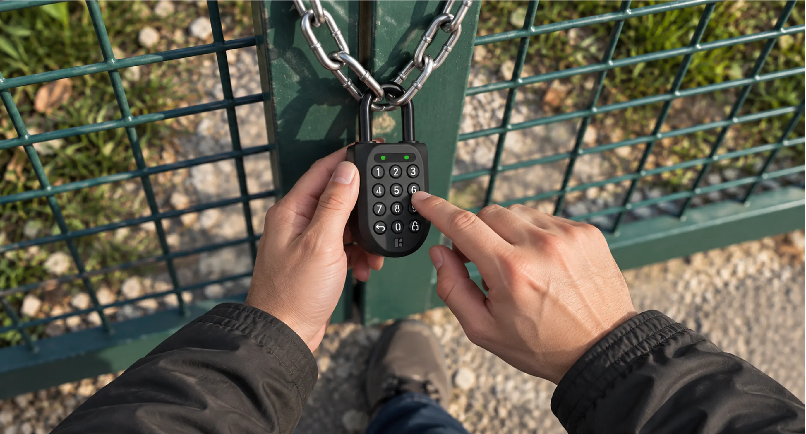 A hand entering a PIN on an igloo Padlock 2 chained across a green mesh gate